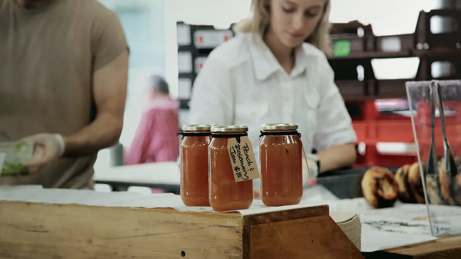 Bocaux de confiture posés sur l’étal d’un marché, artisans en arrière-plan