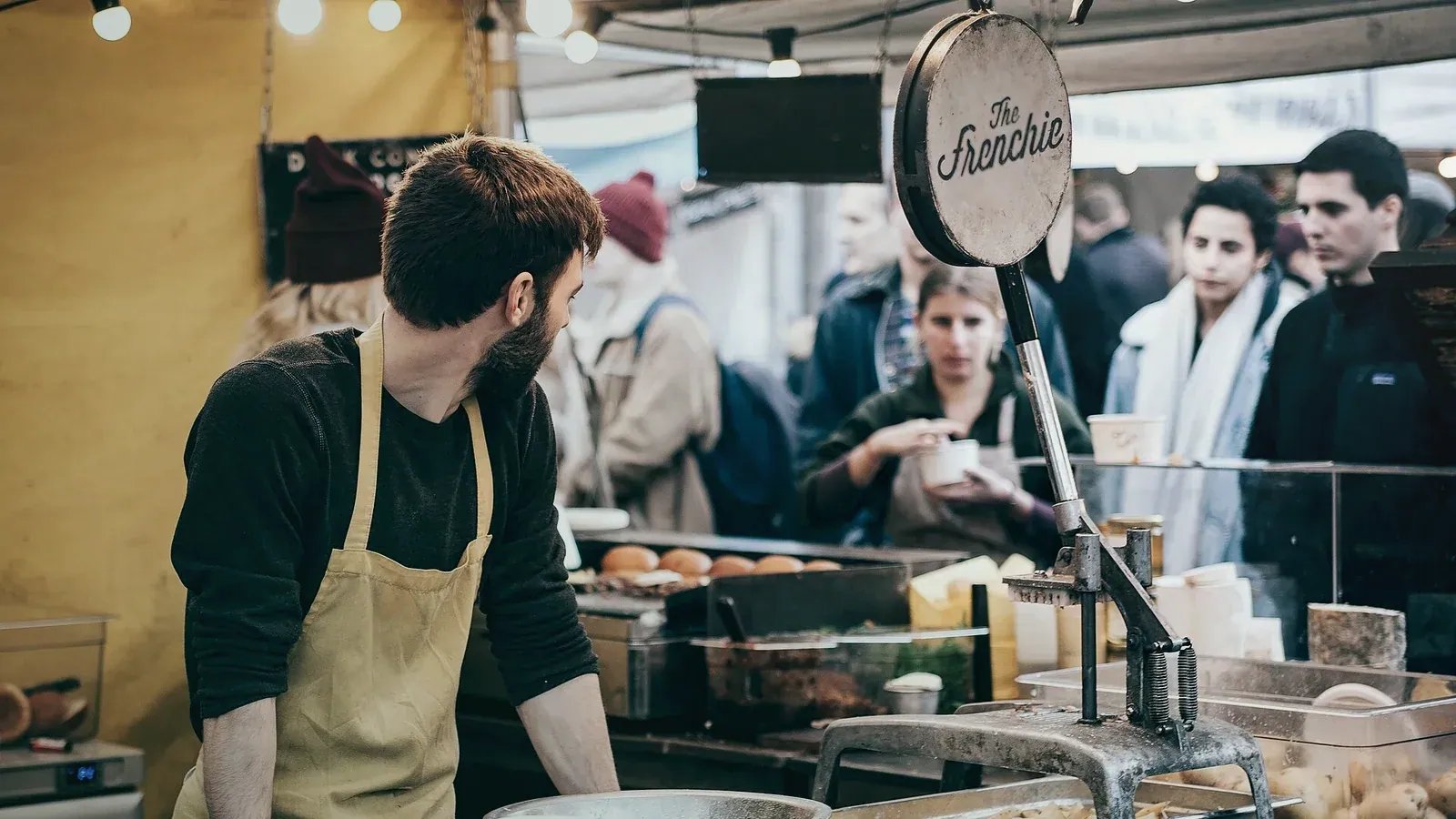 Commerçant en tablier servant ses clients derrière un stand de marché