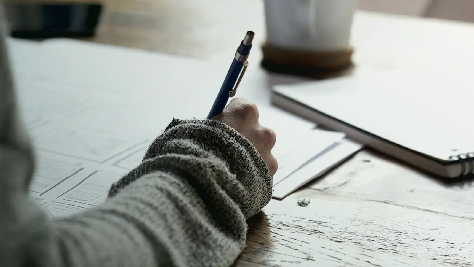 Main qui prend des notes dans un carnet posé sur un plan de travail