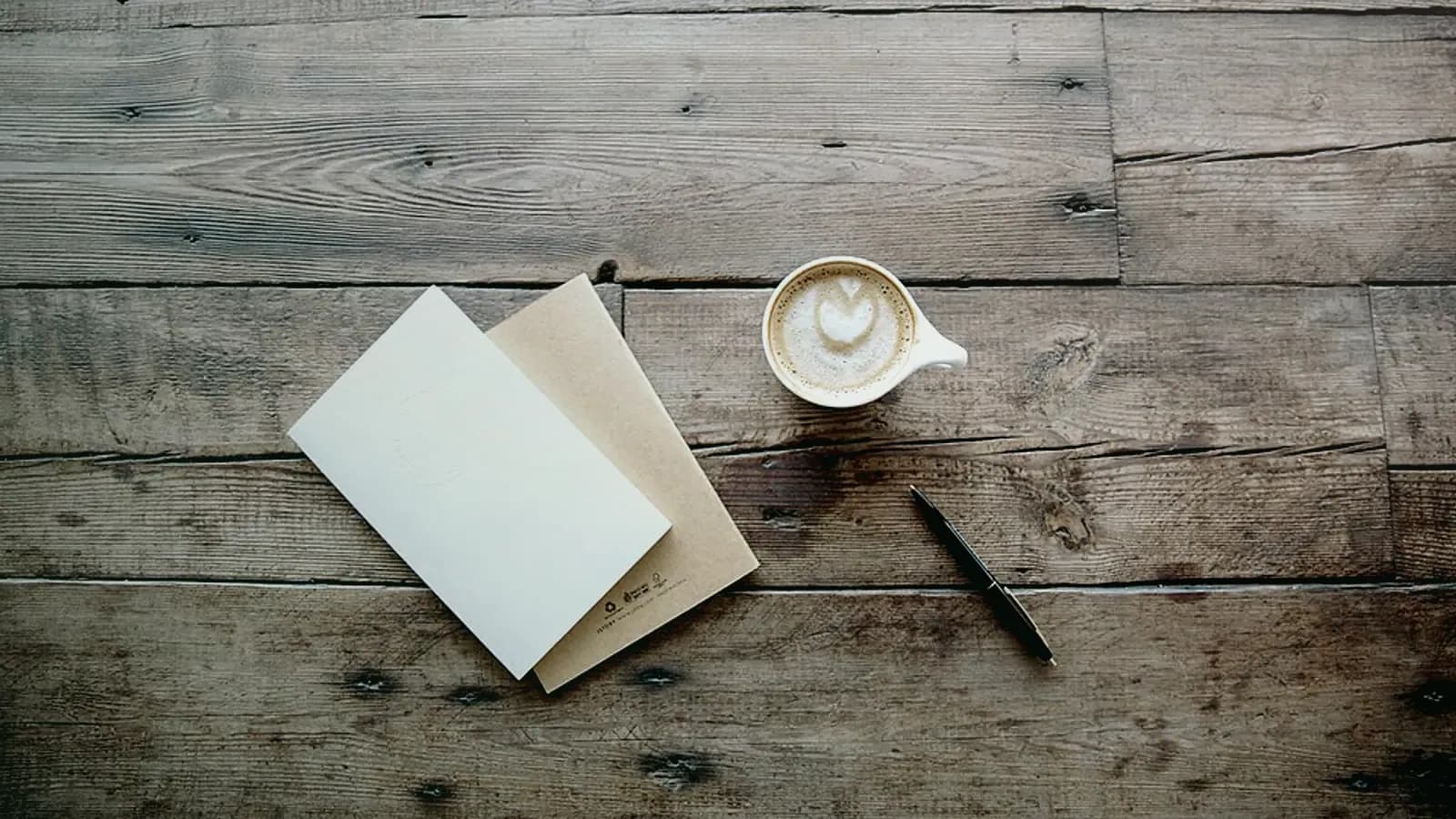 Carnet fermé, crayon et cappuccino posés sur une table en bois brut