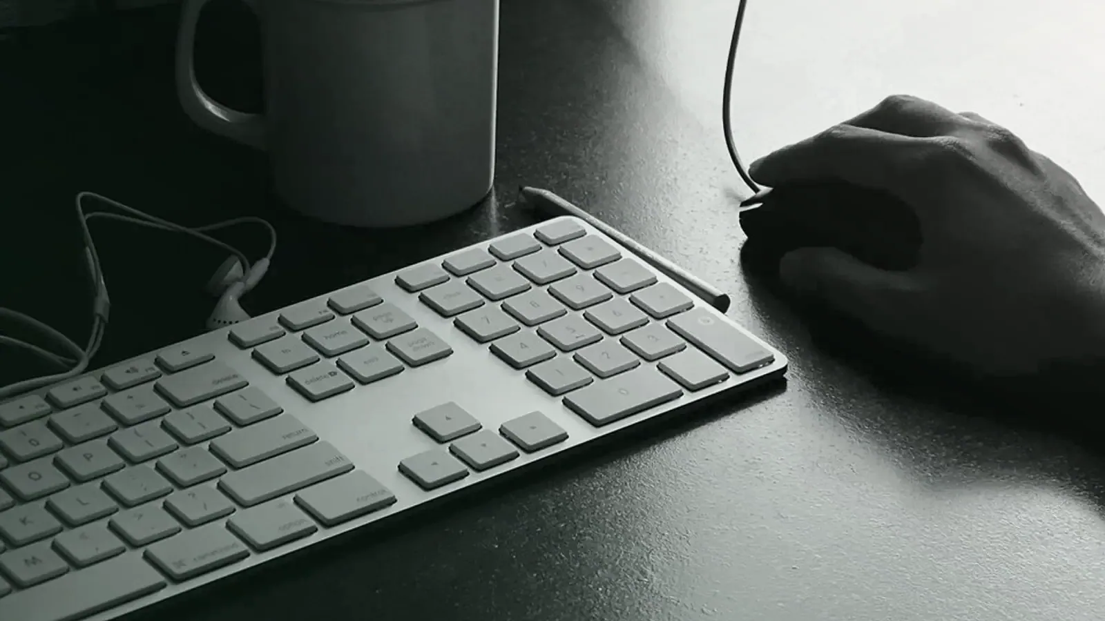 Main sur une souris à côté d’un clavier, en noir et blanc