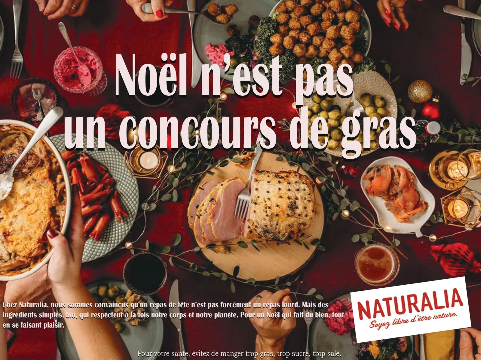 Affiche publicitaire au format 4x3 : table de fête photographiée en plongée, nappe rouge, plats, bougies et branchages, surmontée d’une accroche en grandes capitales blanches et d’un pavé de texte en pied d’affiche