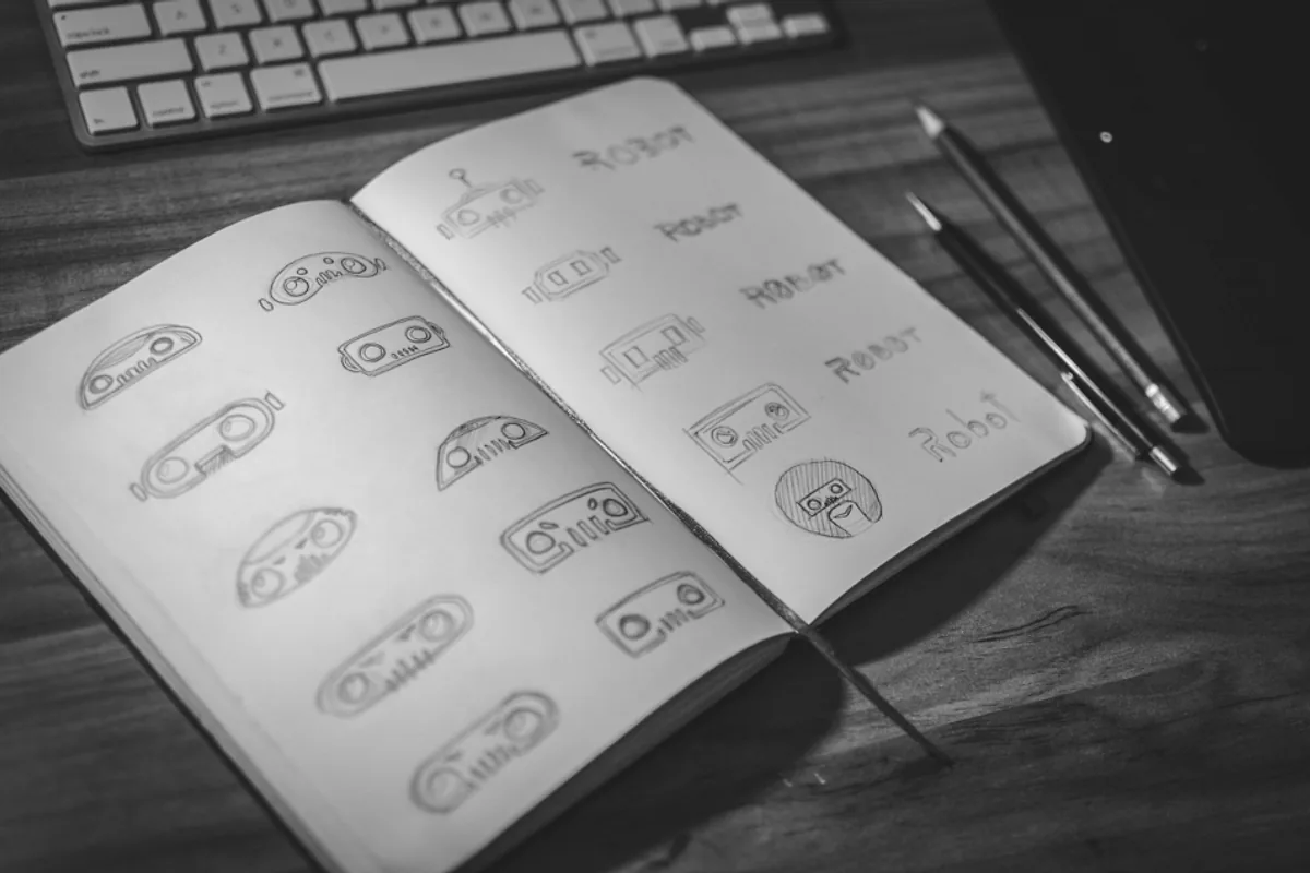 Carnet ouvert sur une planche de recherches de logo dessinées au crayon, à côté d'un clavier et de crayons de graphiste