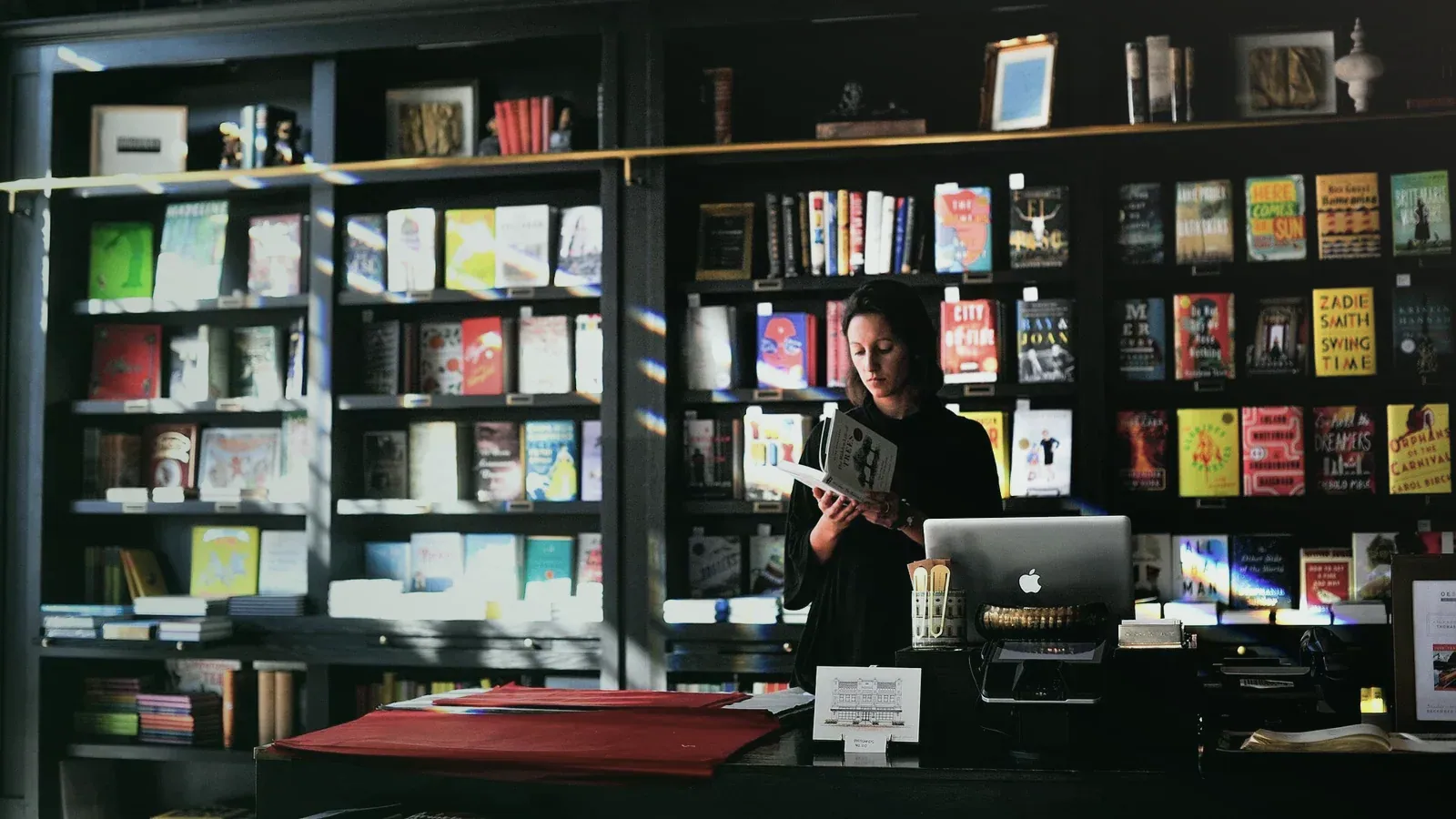 Libraire derrière son comptoir devant des rayonnages remplis d’ouvrages