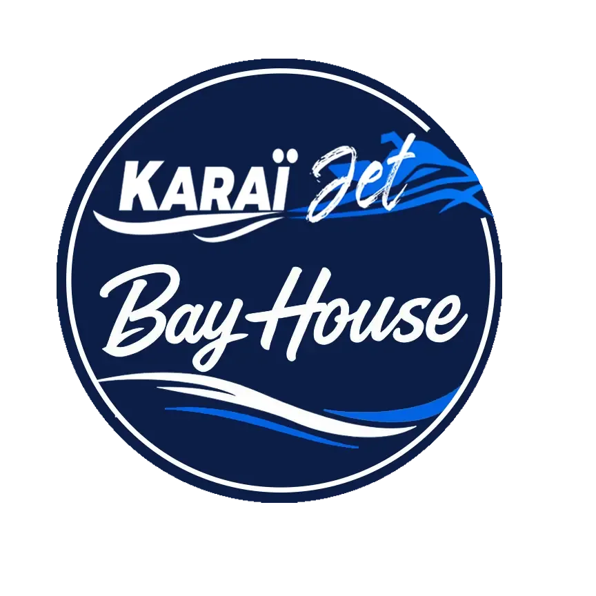 Logo circulaire KaraïJet Bay House sur fond bleu marine, avec la silhouette d’un jet ski, un lettrage manuscrit blanc et deux vagues stylisées bleu et blanc