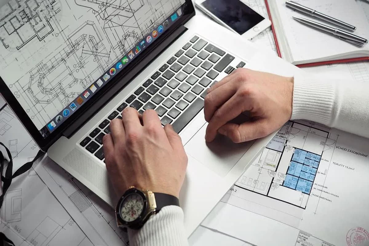 Mains sur le clavier d'un ordinateur portable posé au milieu de plans imprimés, pour préparer la refonte complète d'un site web existant