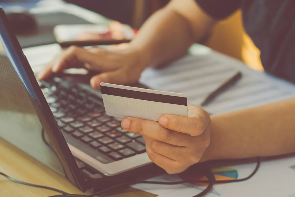 Personne tenant une carte bancaire devant un ordinateur portable pour régler une commande sur une boutique en ligne